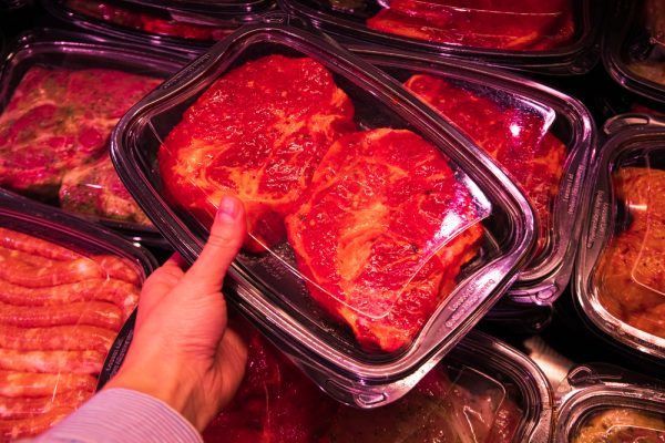 Female hand holds container with meat, meat in supermarket